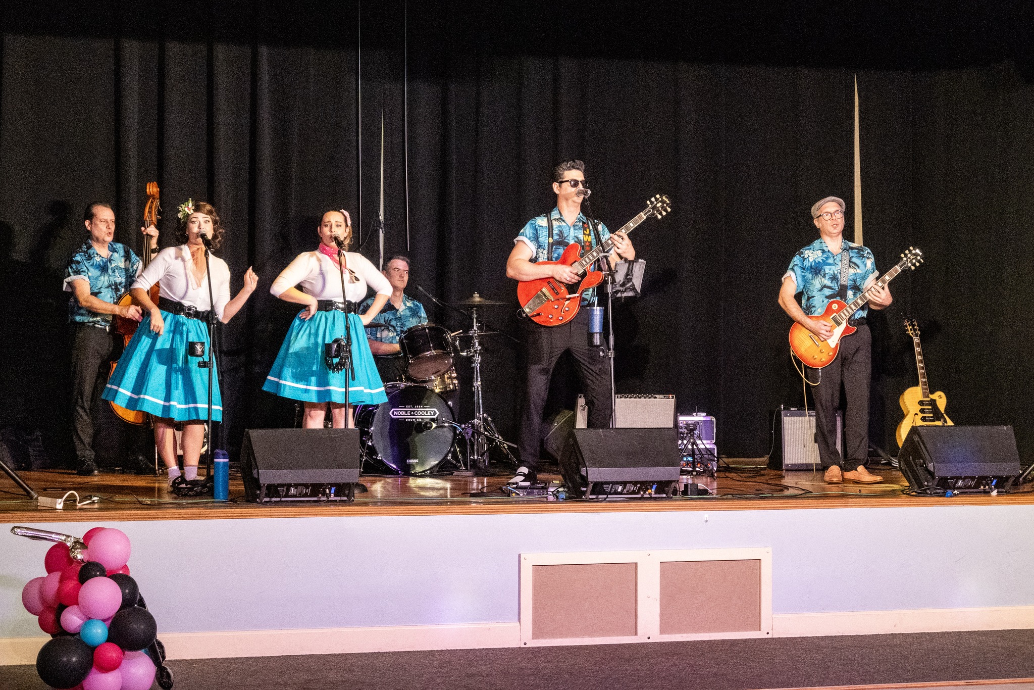 The six-piece band plays on stage Two attendees, one in a pink poodle skirt, dance together at the Senior Citizens Prom in Mount Dora. The girls are wearing white shirts and sky blue poodle skirts and the guys are in matching blue shirts and black pants.
