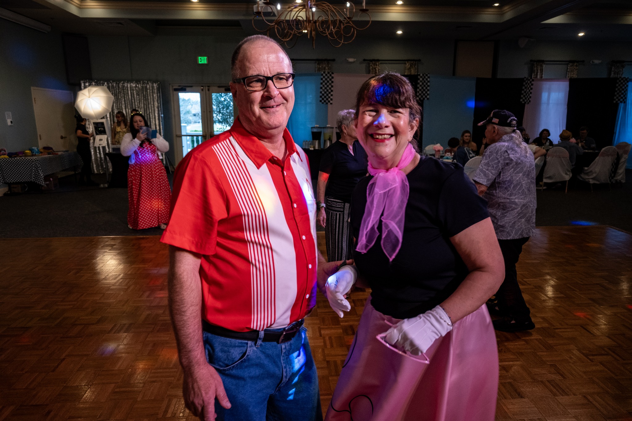Two attendees, one in a pink poodle skirt with a matching pink scarf and the other in a red shirt and jeans, dance together at the Senior Citizens Prom in Mount Dora.
