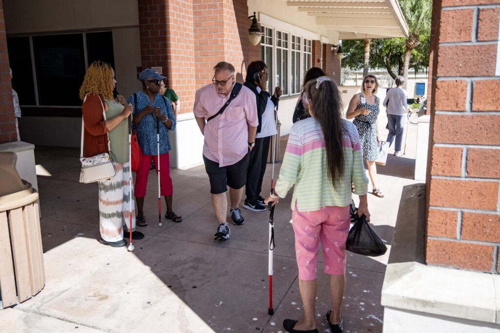 Clients and staff from New Vision wait in the shade outside the Leesburg Library after walking there from Brick and Barrell.
