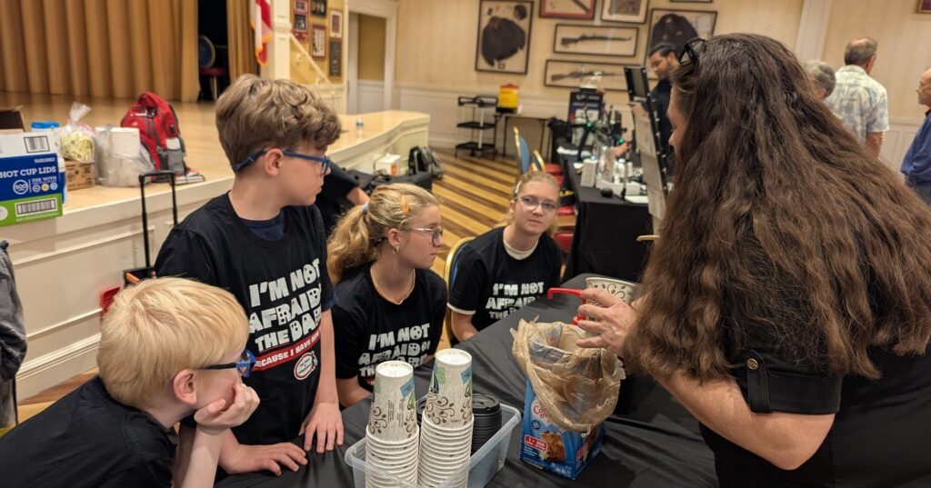 New Vision's Jayne instructs the older kids on the children's program how to serve coffee as the event begins.