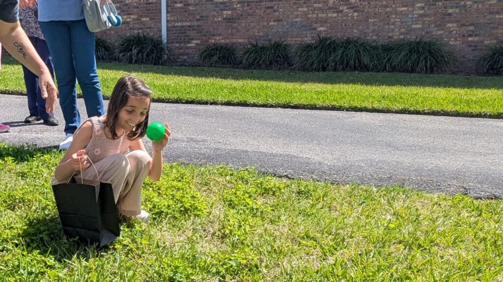 A girl smiles as she holds up a green Easter egg after finding it during the Beeping Egg Hunt.