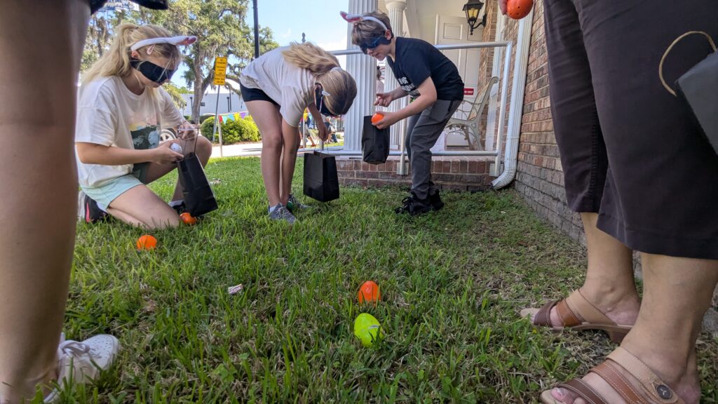 A group of kids listens and hunts for beeping Easter eggs on the lawn outside New Vision's office during the Beeping Egg Hunt.