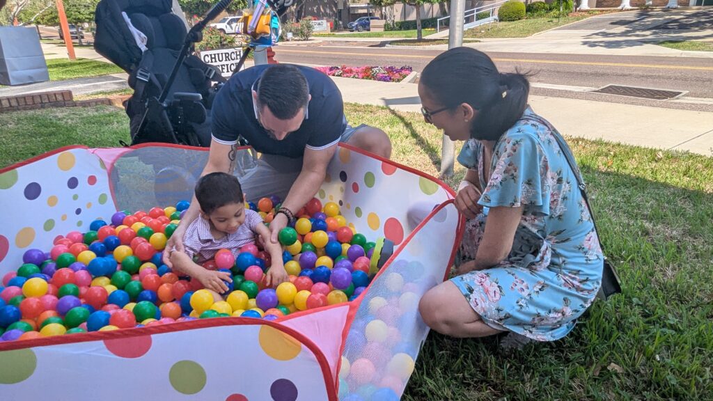 A boy searches for beeping eggs in the ball pit while his parents watch and assist during the Beeping Egg Hunt.