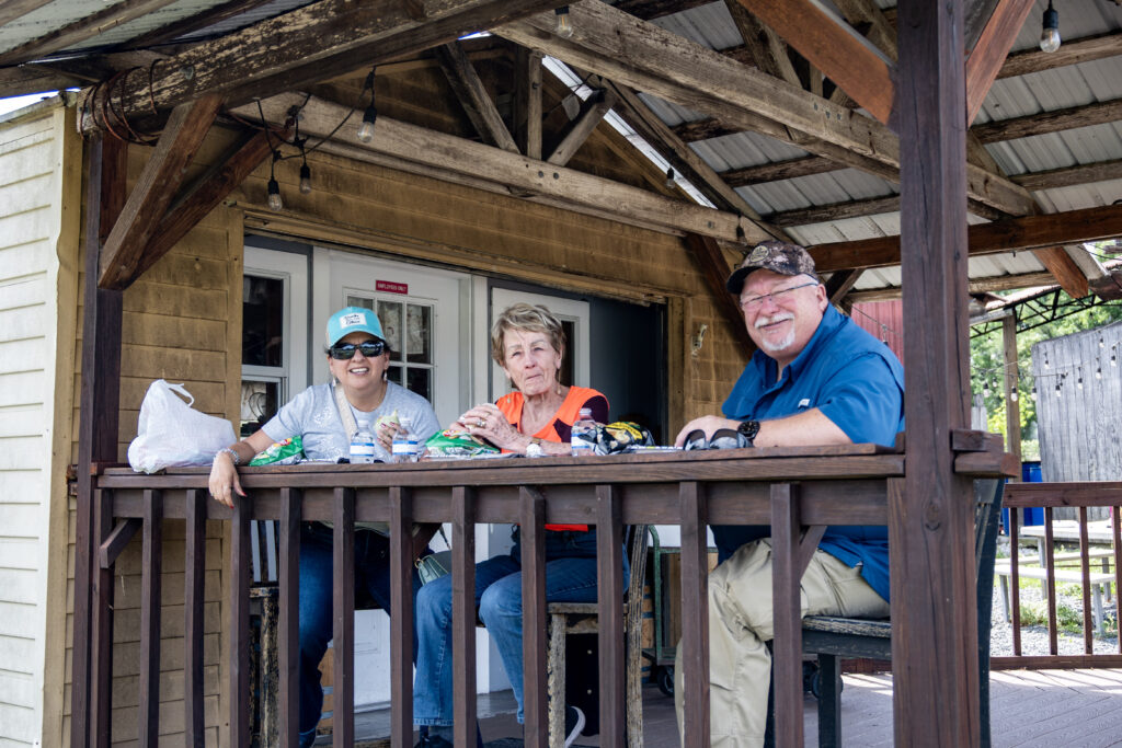Three people sit down for lunch on a porch at Blue Bayou Farms.