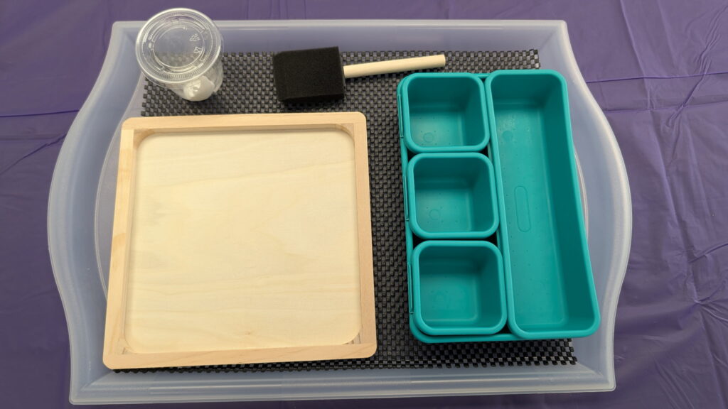 One of the prepared mosaic art kits, which consists of a plastic tray, a wooden frame, a sponge brush, a container of glue, and multiple containers to sort and hold tiles.
