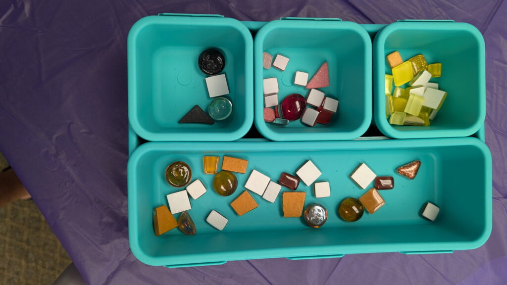Containers from one of the art kits hold various tiles; blue in the top left, pink and red in the top middle, yellow in the top right, and orange along the bottom.

