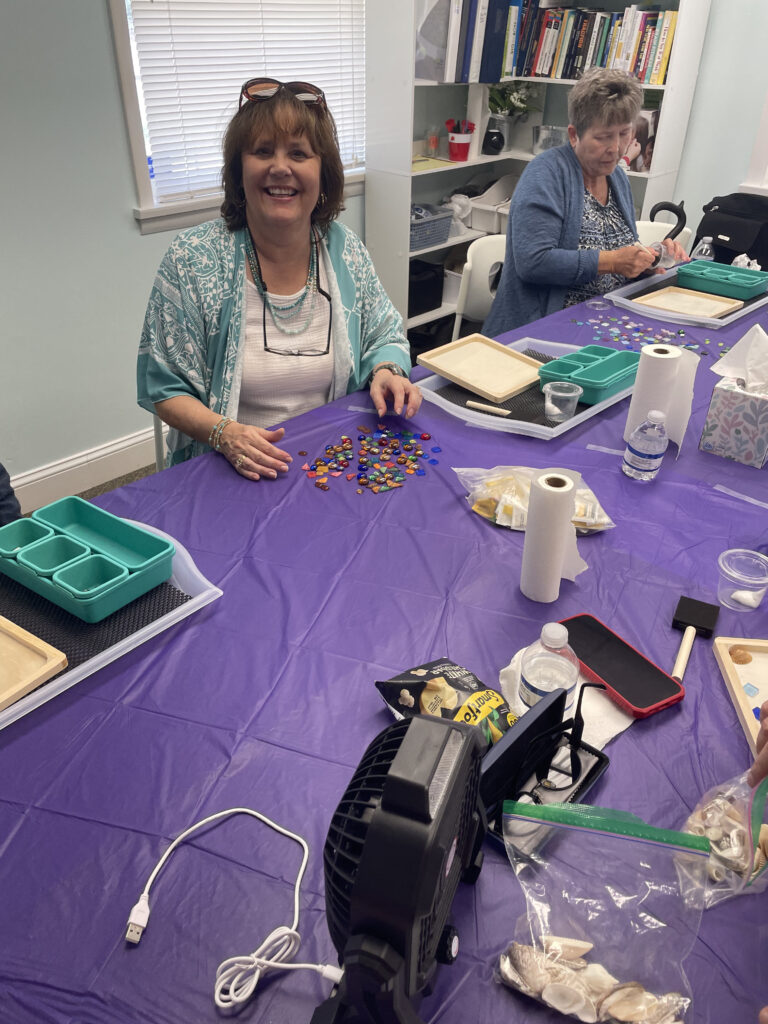 A New Vision client sits at a work table, sorting tiles, and smiles for a picture.
