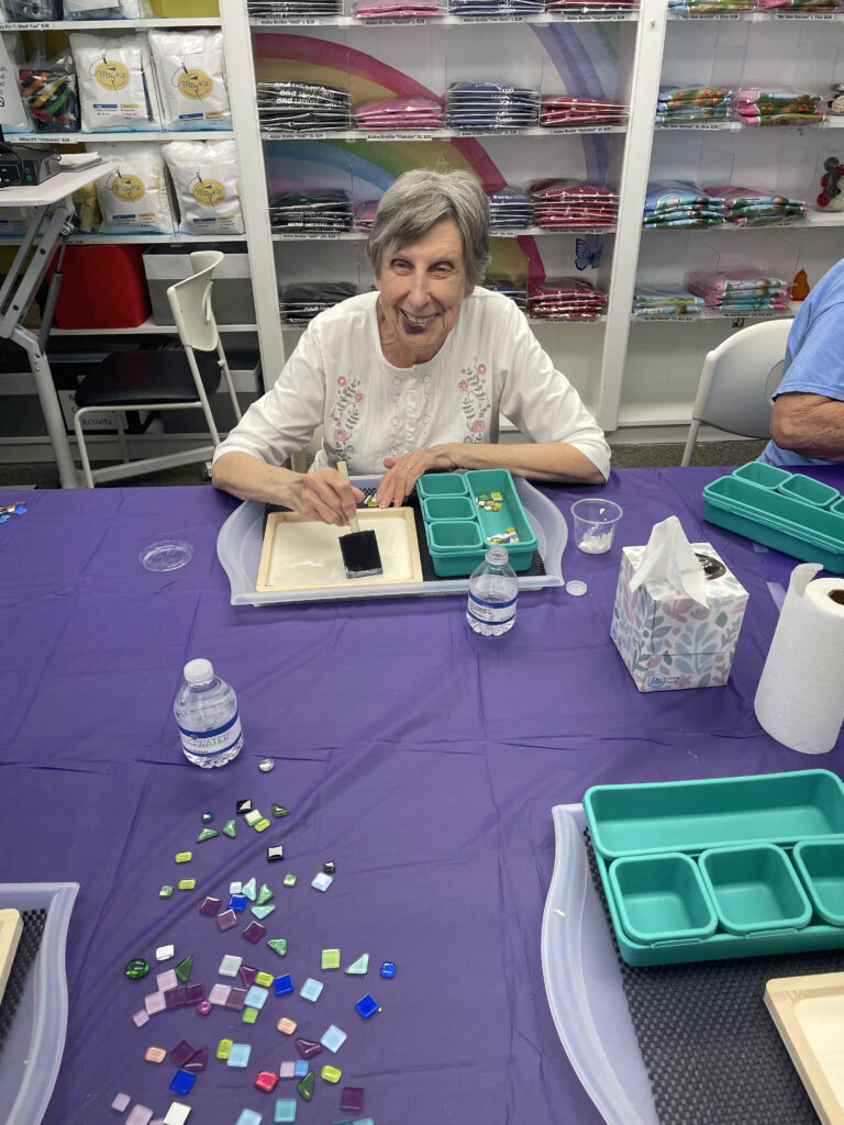 A New Vision client sits at a work table, spreading glue on the wooden frame with a sponge brush, and smiles for a picture.
