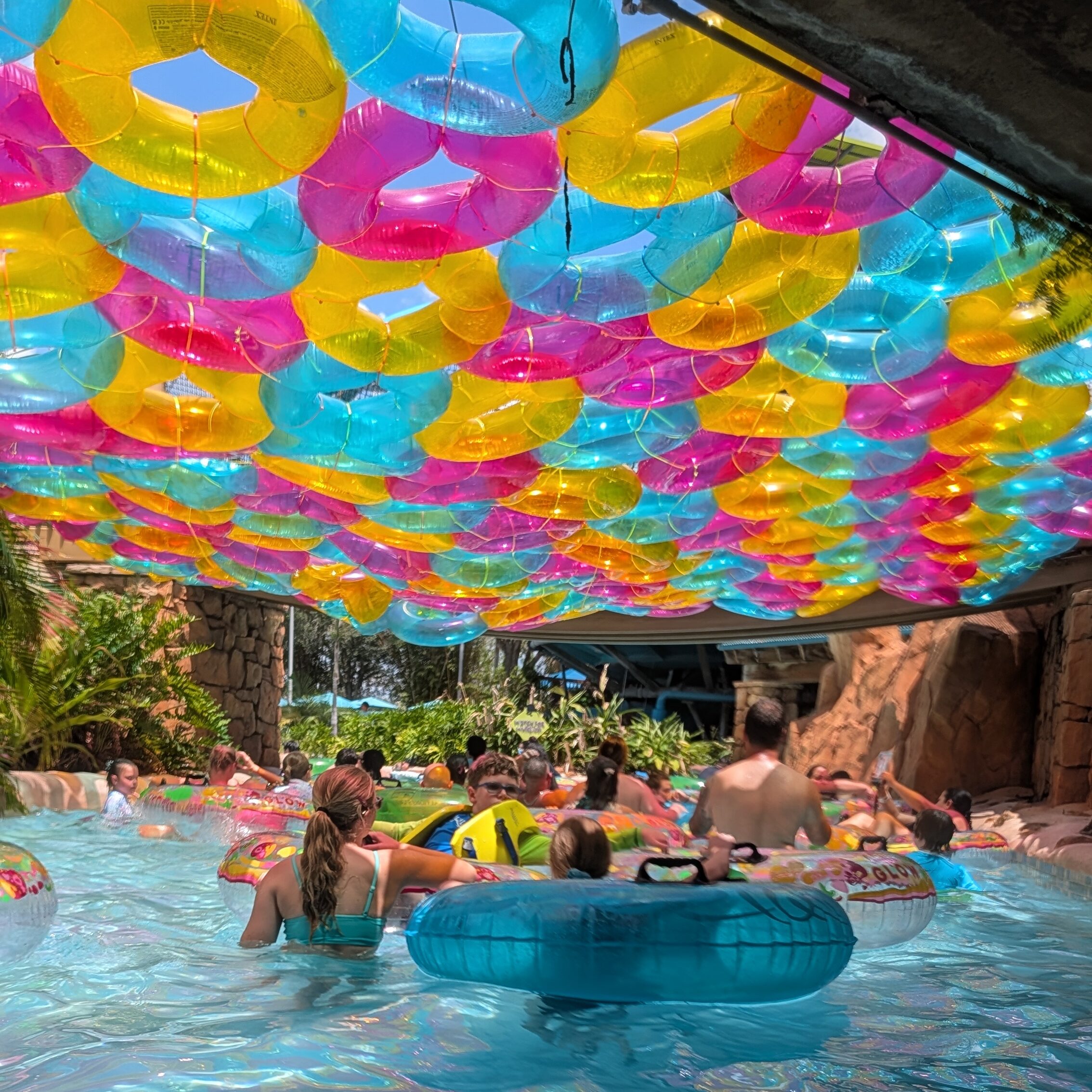 A crowded lazy river at Aquatica Orlando filled with people floating in inner tubes. The group of New Vision kids are seen enjoying the water in the center of the frame amid several people. 