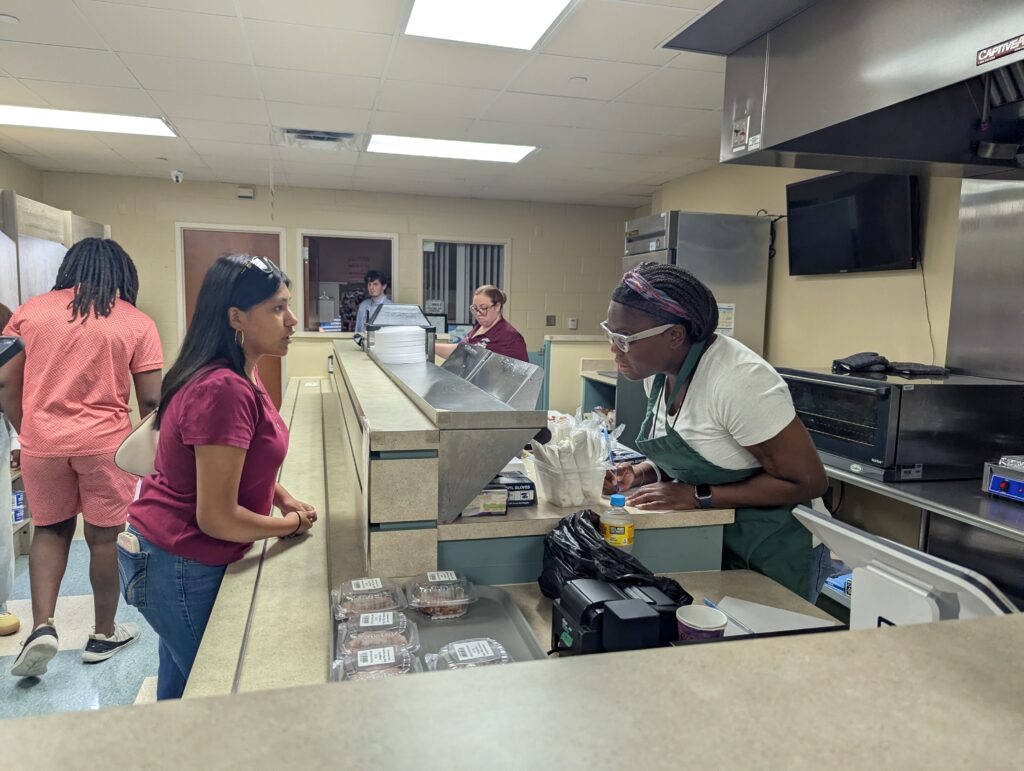Gisele, a teen client of New Vision for Independence, speaks with a worker behind the counter at the campus snack bar, where food-service skills and employment opportunities are put into practice.