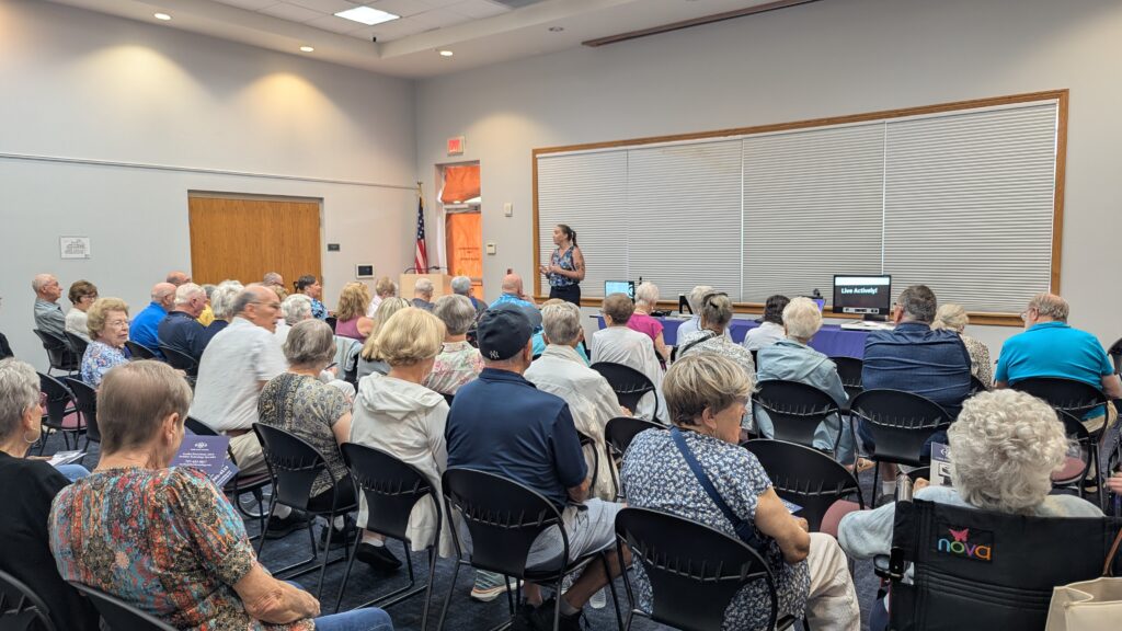 Attendees fill a Leesburg Library meeting room as Annika, a Florida Vision Technology representative presents assistive technology devices during New Vision for Independence's Assistive Technology Expo.