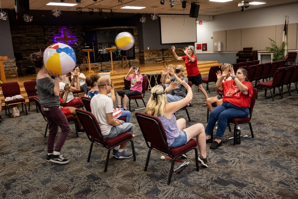 Two beach balls fly through the circle at once as seated participants reach up during an energetic round of accessible chair volleyball.